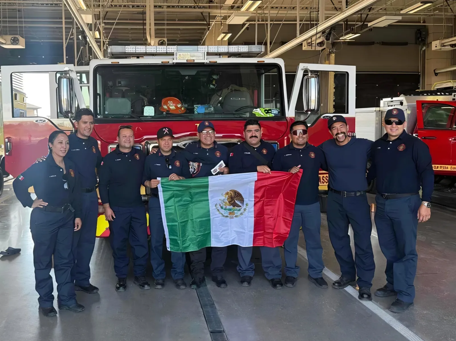 Austin Bomberos members holding the Mexican flag in front of a fire engine
